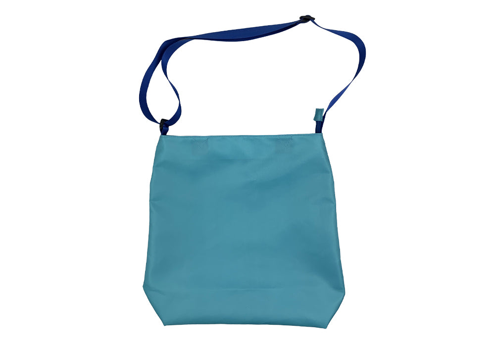 The Electric Picnic Tote Bag by Electric Picnic is a light blue rectangular shoulder bag with a wide, adjustable dark blue strap and minimalist design, shown against a white background. Perfect as a reusable accessory for daily outings.