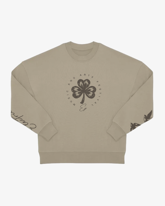Introducing the EP 2026 Click & Collect Vintage Clover Crewneck Natural—a beige crewneck sweatshirt featuring a bold black four-leaf clover graphic and circular “Music and Arts Festival” text on the front, complemented by black printed designs on both sleeves.